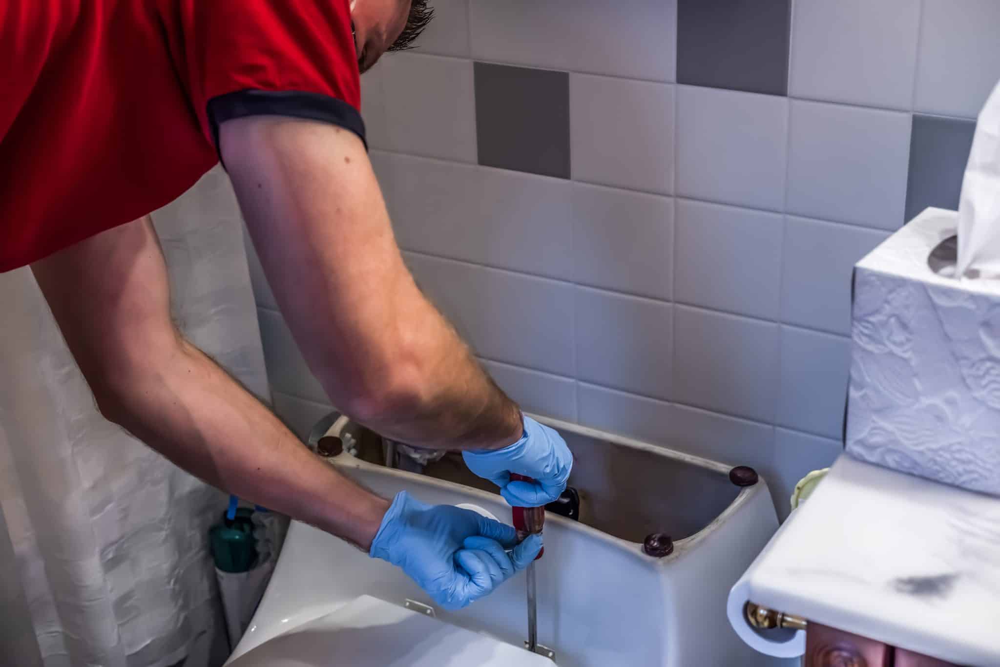 Plumber fixing toilet in bathroom.