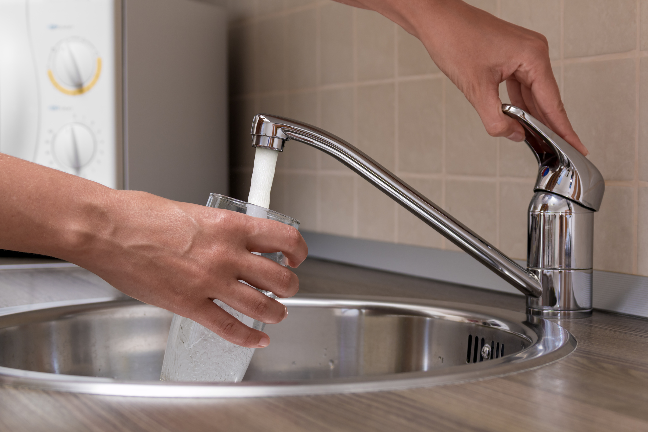 Eco Plumbing, A woman, pouring water from faucet mixer into a glass at a kitchen.