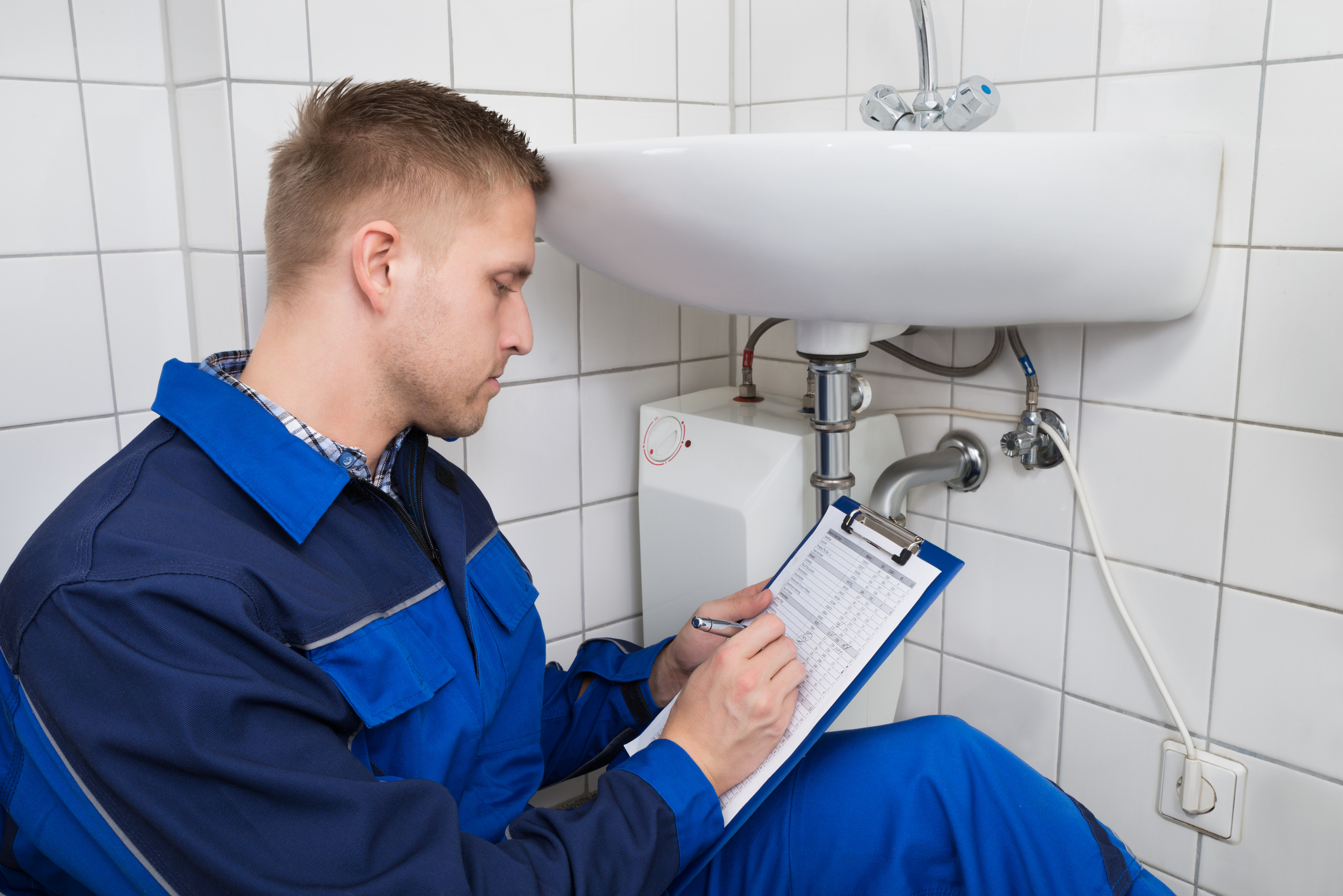 Plumber conducting a regular plumbing audit, writing on a clipboard in the bathroom.