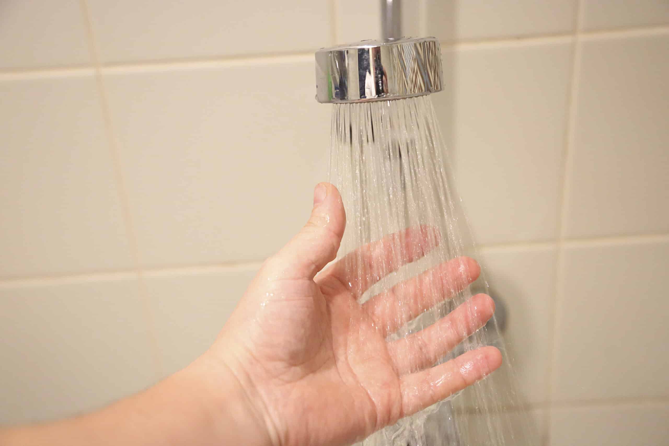 Male hand check water temperature in the shower, Shower Cartridge Replacement.